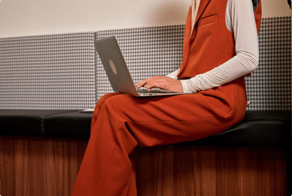 Femmes en entreprise habillée avec un ensemble orange et qui cherche une mutuelle sur son ordinateur de travail